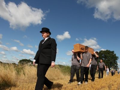 woman leading coffin being carried across field